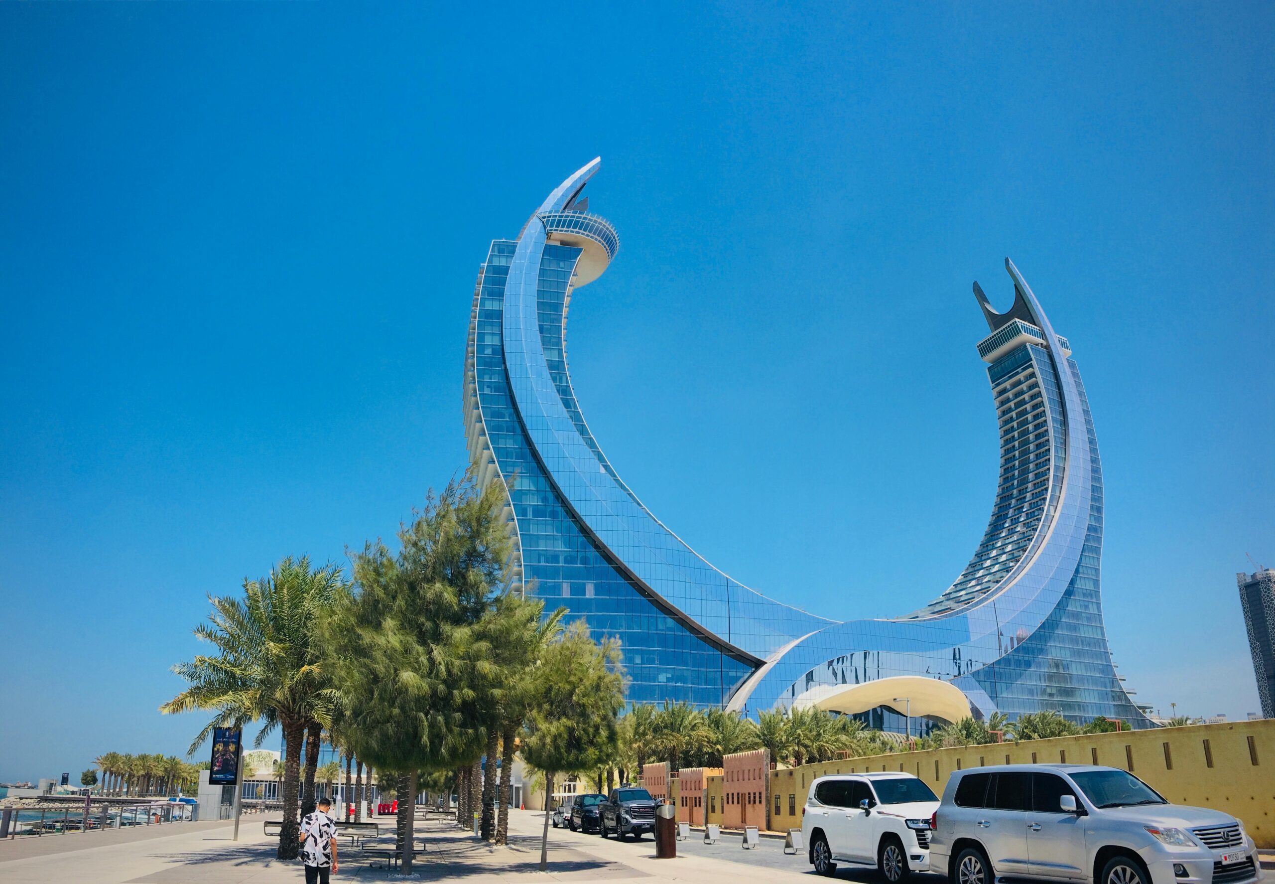 Stunning modern architecture of a luxury hotel in Doha with palm trees and clear blue sky.
